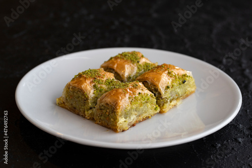 Pistachio baklava dessert on a dark background. Turkish sweet dessert concept. plate of pistachio baklava. sherbet sweet Mediterranean bakery. close up. selective focus.