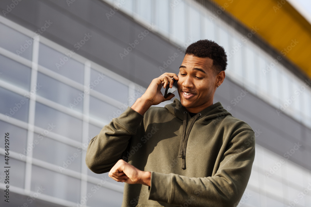 young african american man in casual outfit looking at imaginary hand watch while talking on phone young african american man in casual outfit looking at imaginary hand watch while talking on phone