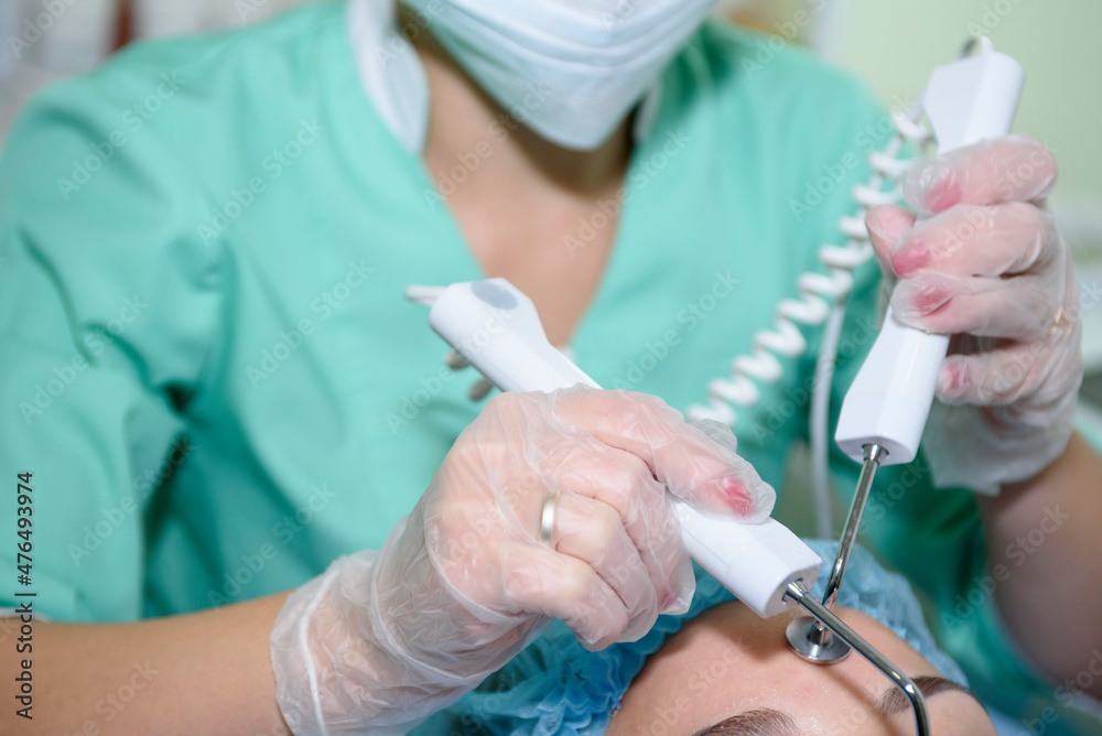 Microcurrent therapy when visiting a beauty salon. Cosmetological innovative procedure. In the background, a beautician treats the face with electrical impulses. Microcurrent therapy when visiting a beauty salon. Cosmetological innovative procedure. In the background, a beautician treats the face with electrical impulses.