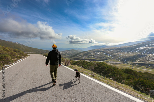 Persona haciendo senderismo por una carretera de montaña con vistas en un día soleado con nubes 