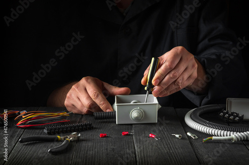 Close-up of hands of a master electrician during work. Installing a cable or wire to grey junction box. Idea for the installation and repair of electrical equipment