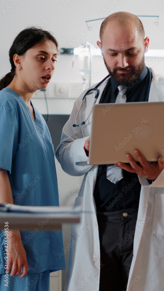 Obraz premium Doctor doing consultation with retired patient in bed. Medic with laptop talking to nurse about healthcare medicine before examining patient with nasal oxygen tube and heart rate monitor