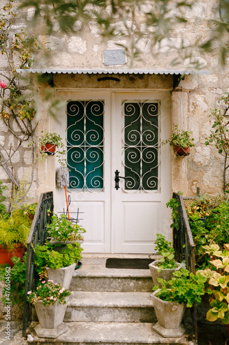 Threshold of an old stone house with a wooden door with a forged lattice and flowers in pots