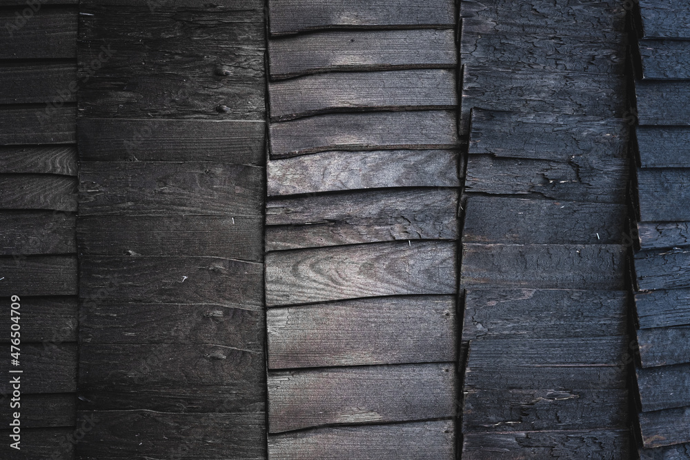 Black burnt wooden texture background. Beautiful, stylish boards pattern with optical illusion of movement and ombre effect. Igloo sauna or house exterior design. Harsh wood without finish. Copy space