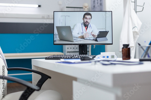 Computer screen with remote doctor having online videocall meeting conference standing on table in empty hospital office. Telework videoconference call during medical consultation. Medicine concept