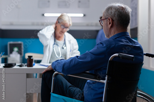 Close up of man with physical disability attending checkup appointment with medic. Aged patient with illness sitting in wheelchair while meeting with specialist to receive medical advice.