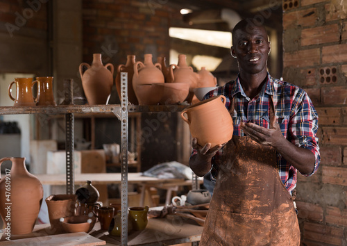 Foto Smiling afro craftsman offering for sale different stoneware and ceramic product