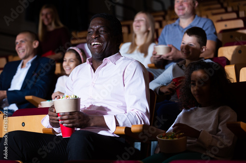 Εκτύπωση καμβά Portrait of cheerful laughing african american man sitting in movie theater with popcorn and watching comedy
