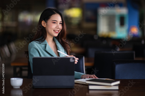 Portrait of Smiling a beautiful young Asian businesswoman sitting with laptop and computer while doing some paperwork at the out office. 