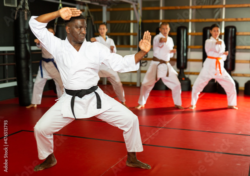 African-american man in kimono standing in fight stance during group karate training.