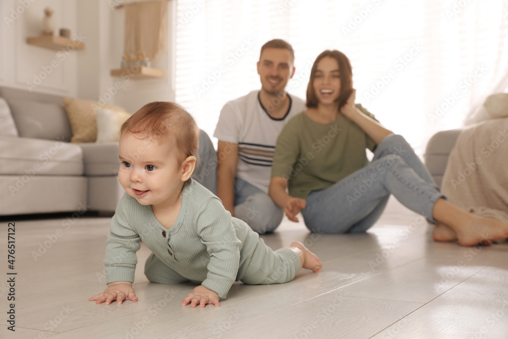 Happy parents watching their cute baby crawl on floor at home Happy parents watching their cute baby crawl on floor at home