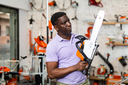 African-american man choosing chainsaw in gardening tools store.