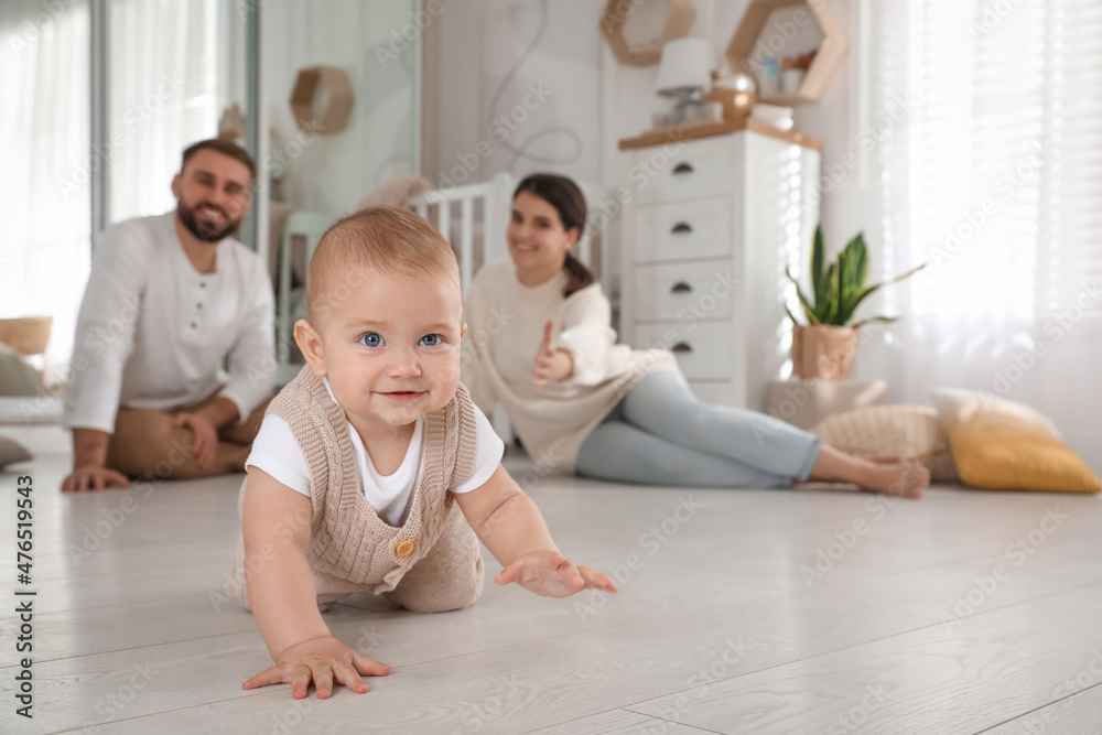 Happy parents watching their baby crawl on floor at home Happy parents watching their baby crawl on floor at home