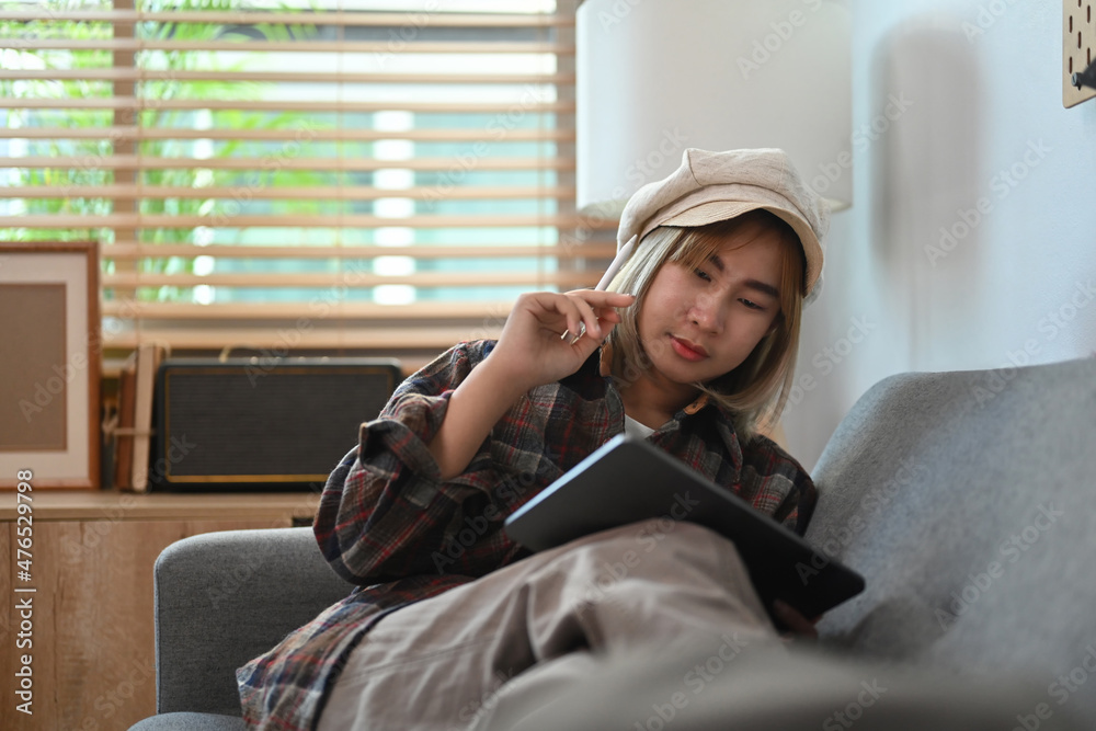 Young asian woman sitting on comfortable couch and using digital tablet. Young asian woman sitting on comfortable couch and using digital tablet.