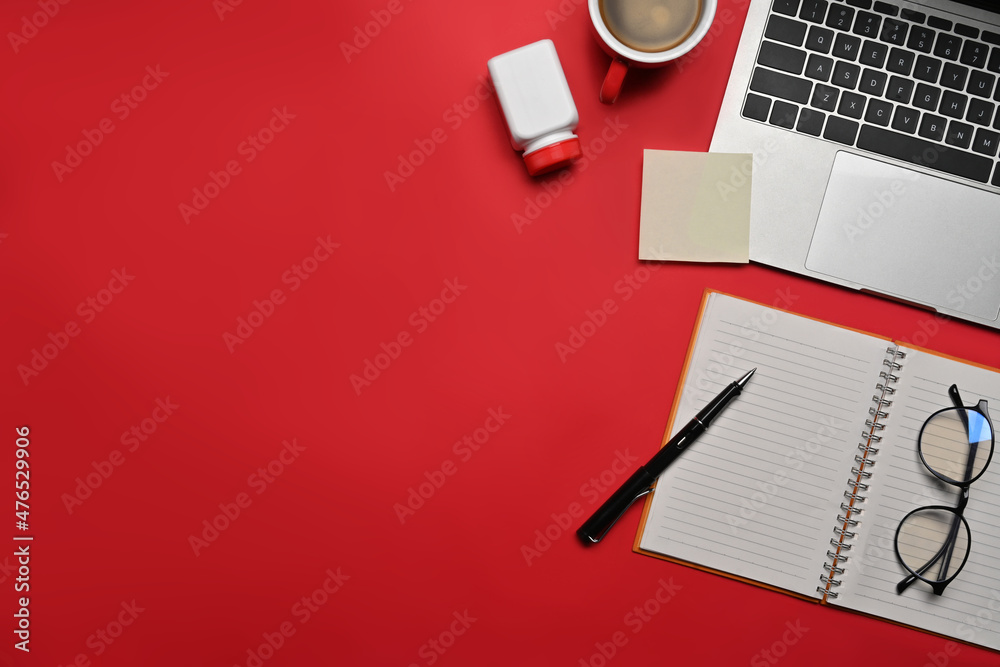 Top view computer laptop, notebook, glasses and pill bottle on red background.