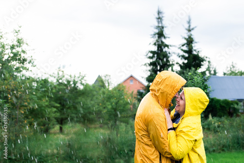 A married couple in yellow raincoats in the rain in their backyard. Front view. © Anastasiia