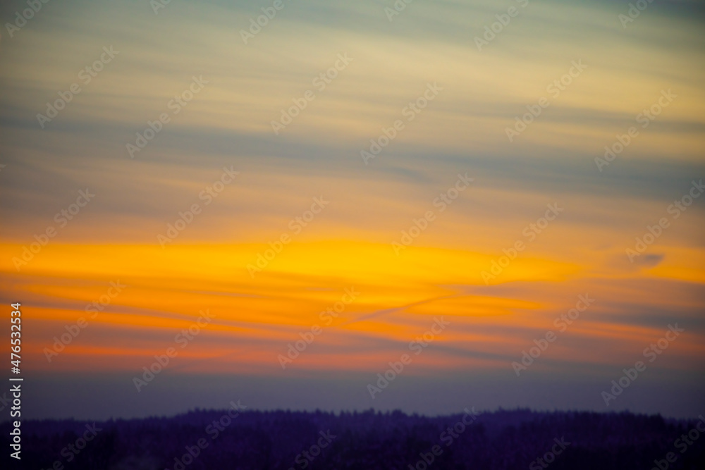 Blurred evening sky wallpaper. Bright orange and yellow sunset, thin textured clouds, the beauty of winter weather. Selective focus on the details, defocused background.