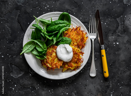 Potato latkes with sour cream and spinach salad on a dark background, top view