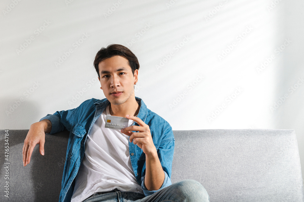 A young handsome cool man is confident holding a credit card in his hand he is ready to shop things. An Internet wireless Online technology and online shopping concept idea A young handsome cool man is confident holding a credit card in his hand he is ready to shop things. An Internet wireless Online technology and online shopping concept idea