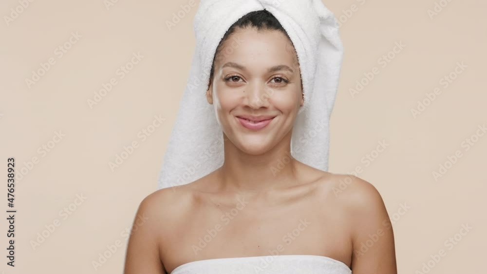 Funny young slim cute African American woman with a towel on her head and bare shoulders throws away orange woman razor smiling wide for the camera on beige background | Unwanted hair removal concept