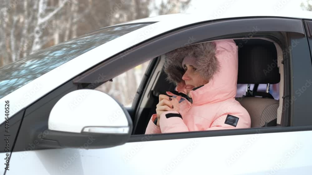 Young Woman in Warm Clothes Blowing on her Hands Trying to Get Warm while Sitting in her Car in Winter Day Young Woman in Warm Clothes Blowing on her Hands Trying to Get Warm while Sitting in her Car in Winter Day