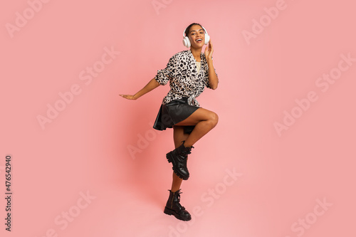 Smiling woman listenning music by earphones , posing on pink background. Wearing stylish blouse and leather skirt. Full lenght.