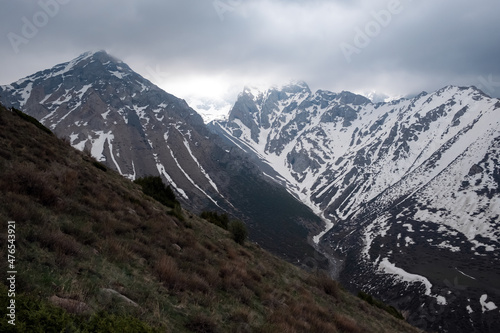 Rocky mountains covered with snow with storm clouds on background. Sayram-Ugam National Park.