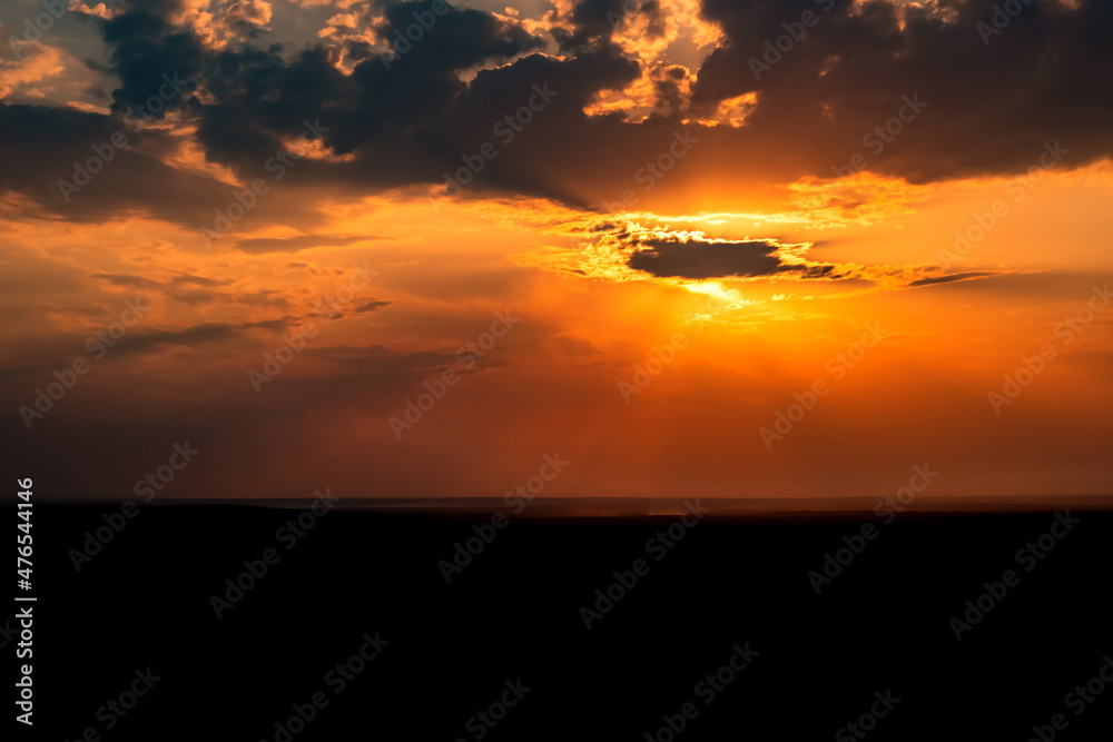 Beautiful golden orange sunset with horison silhouette and sun beams shining through clouds for concept design.