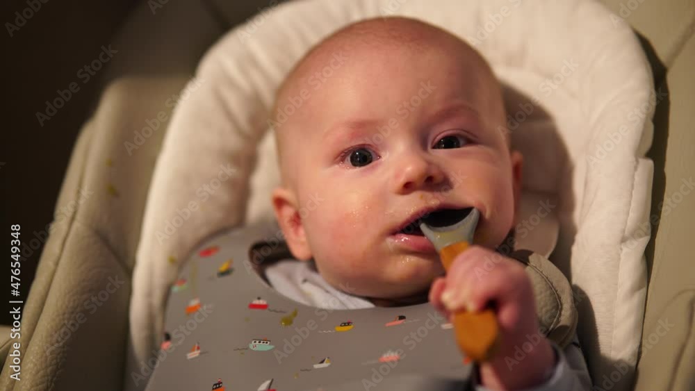 Baby boy sitting on feeding chair gnawing rubber spoon. Cute infant teething and biting spoon after eating. Baby boy sitting on feeding chair gnawing rubber spoon. Cute infant teething and biting spoon after eating.