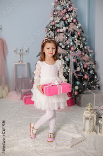 Smiling child girl under Christmas tree with decorations in room.