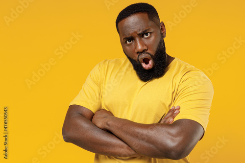 Young shocked angry offended indignant black man 20s in bright casual hold hands crossed folded look camera t-shirt isolated on plain yellow color background studio portrait. People lifestyle concept photo