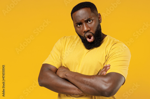 Young shocked angry offended indignant black man 20s in bright casual hold hands crossed folded look camera t-shirt isolated on plain yellow color background studio portrait. People lifestyle concept