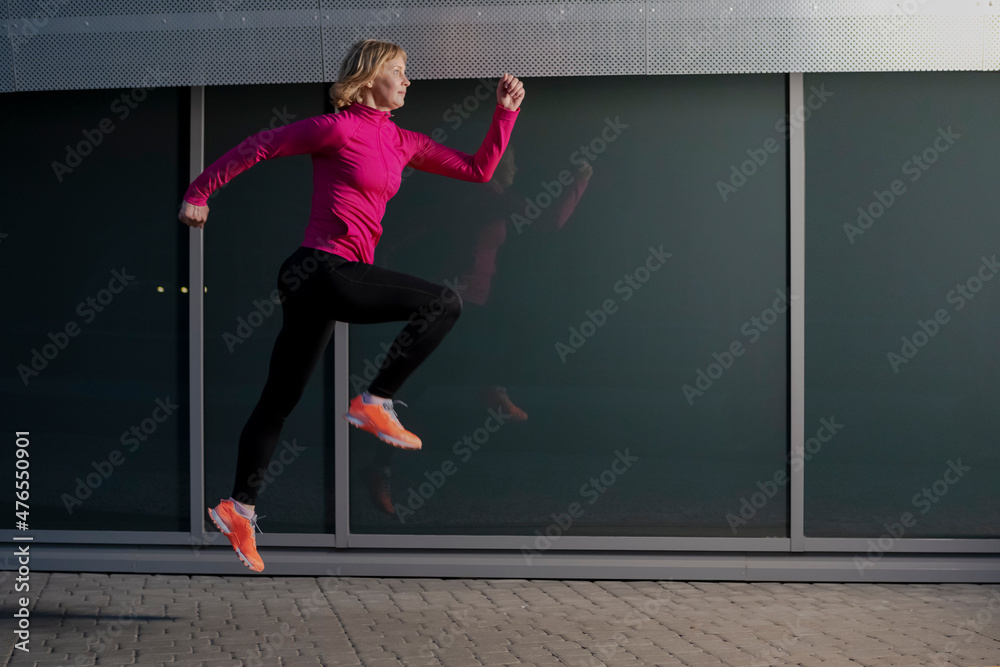 Mature Woman Running in High Jump Outdoors Against Glass Reflective Background
