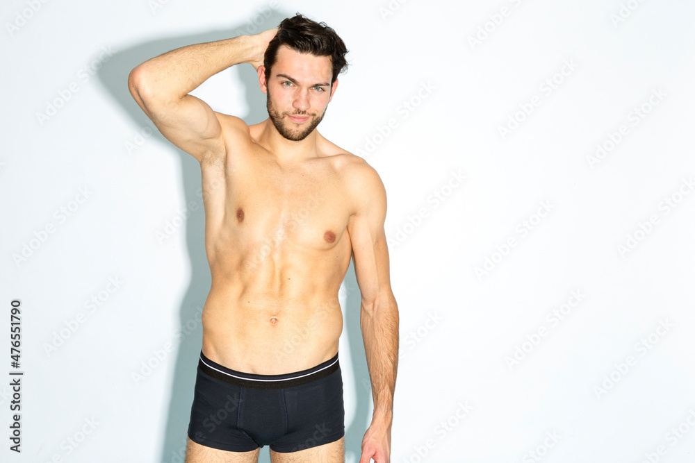 Caucasian Handsome Brunet Man in Black Underware In Good Phyisycal Fit While Posing in Underware While Touching Hair Against White