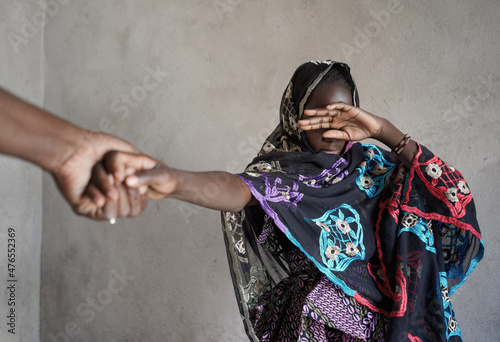 Veiled black African girl with her hand covering her eyes, pulled by the hand of an adult towards an atrocious fate; girl child abuse concept photo