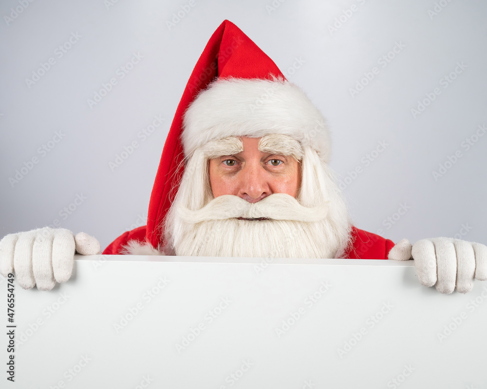 Naklejka premium Santa Claus peeks out from behind an ad on a white background. Merry Christmas.
