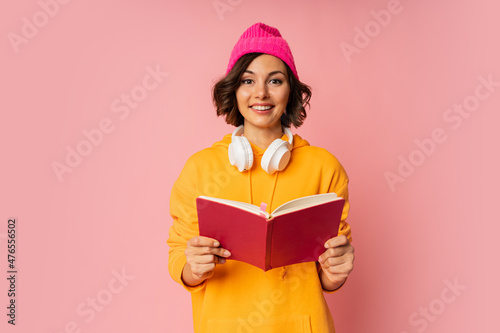 Studio photo of happy cute student with notebooks and earphones standing over pink background. Education  concept.