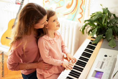 Woman and girl playing a piano. Beautiful mom teaching her daughter playing a piano..