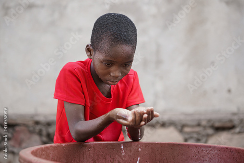 Fototapet Little black African boy fetching water with his cupped hands from a tub to wash