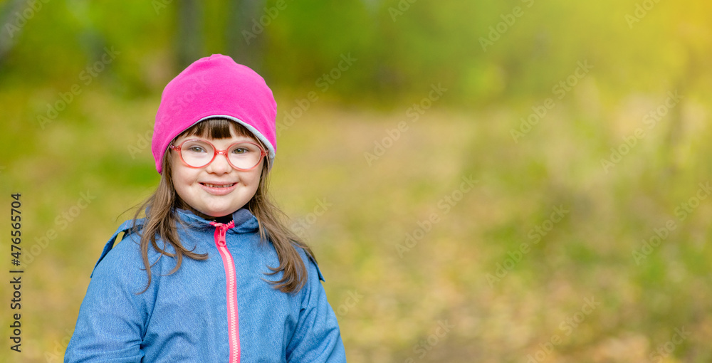 Smiling young girl with Downs syndrome stands at autumn park. Empty space for text Smiling young girl with Downs syndrome stands at autumn park. Empty space for text