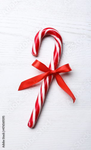 Sweet Christmas candy cane with bow on white wooden table, top view