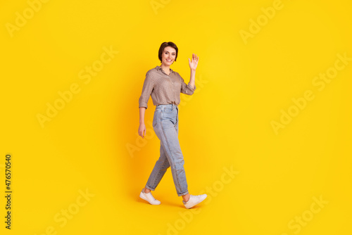 Full body profile side photo of young attractive woman walk waving hi arm isolated over yellow color background