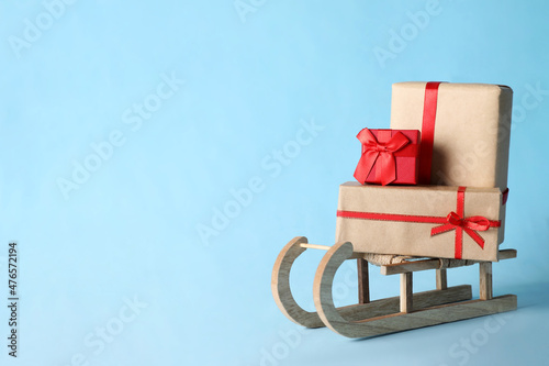 Wooden sleigh with Christmas gift boxes on light blue background, space for text