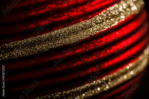 Close up of a red patterned Christmas bauble with glitter stripes. Tree decorations in red and gold.