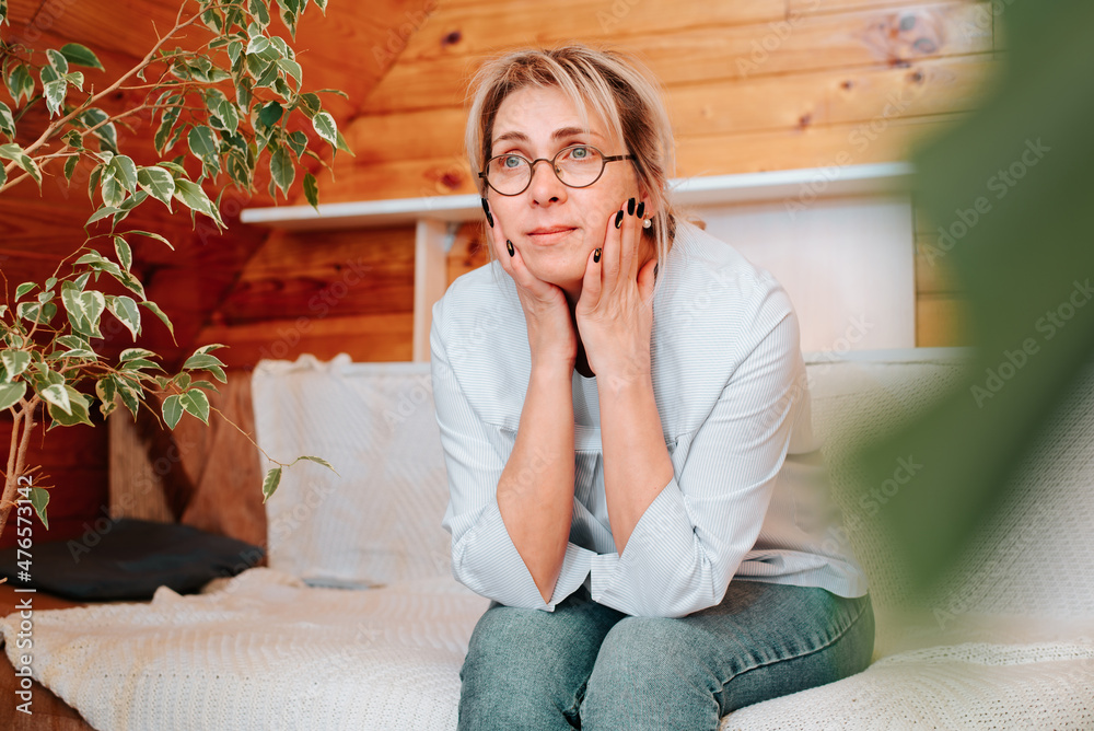 Adult lonely sad woman sitting on sofa and looking away, indoors. Middle aged caucasian woman wearing glasses and casual clothes alone at home. Loneliness, sadness, stress concept Adult lonely sad woman sitting on sofa and looking away, indoors. Middle aged caucasian woman wearing glasses and casual clothes alone at home. Loneliness, sadness, stress concept
