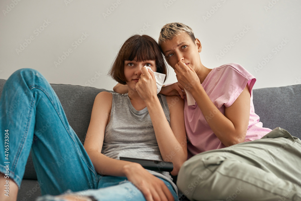 Sad lesbian girls watching TV and crying on sofa