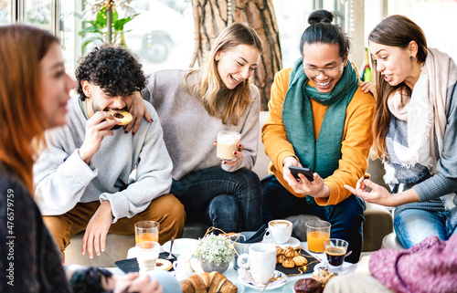 Multicultural friends playing with mobile phone at coffee bar - People having fun together at cafeteria on brunch time - Life style concept with happy men and women at cafe venue - Bright warm filter