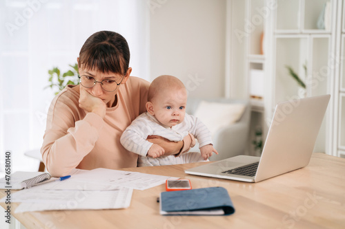 Young upset mother frustrated with financial problems, trying to find a solution while babysitting with her little child. Single unhappy mom looking at documents, tired of motherhood difficulties