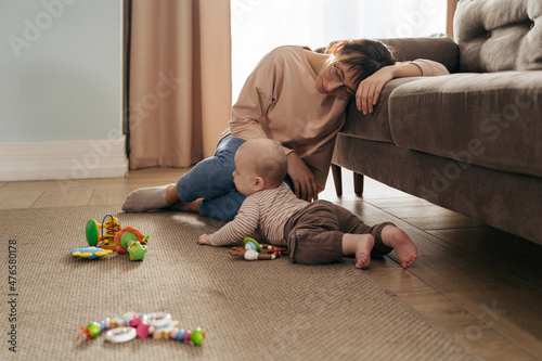 Young exhausted mother is very tired, fell asleep on sofa near her playing infant baby, suffering from postpartum depression, difficulties of motherhood, sleepless nights.
Mom's trying to take a nap photo