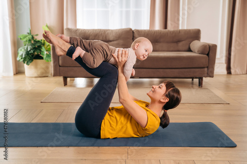 New mom lifting her adorable little baby with her legs, doing post-natal fitness exercise. Sports mother is engaged in fitness and yoga with a baby at home. Healthy motherhood and postpartum recovery photo